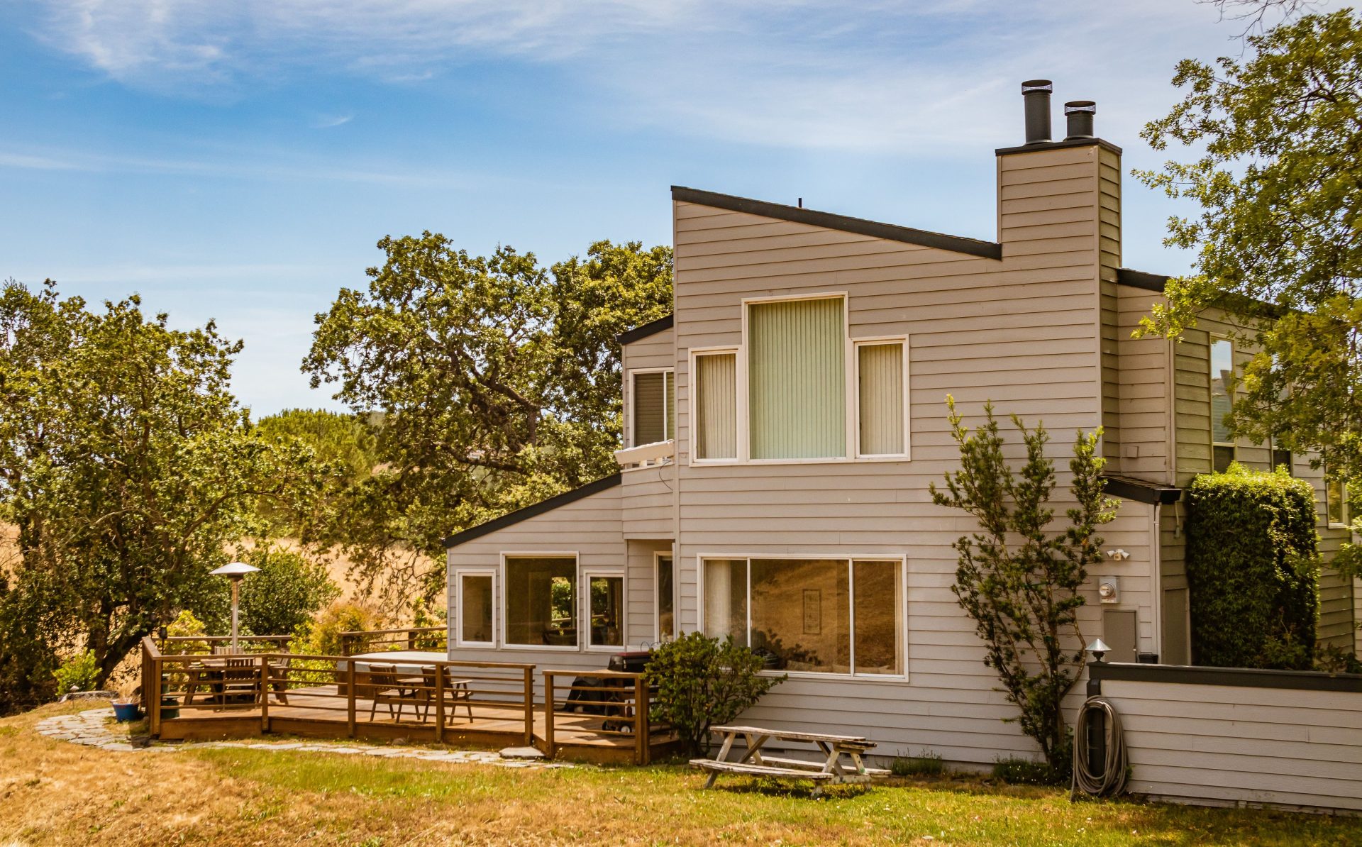Contemporary suburban house featuring large glass windows and a spacious deck in a lush outdoor setting.